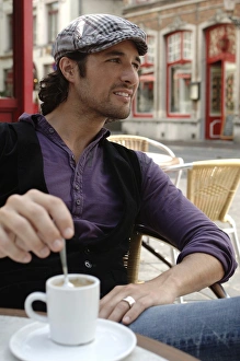 Man, early 30s, wearing casual clothes sitting in an outdoor cafAA stirring a coffee cup Man, early 30s, wearing casual clothes sitting in an outdoor cafAA stirring a coffee cup