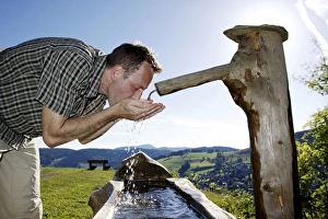 A man in his mid 40 quenches his thirst at a well, Todtnauberg in the Black Forest A man in his mid 40 quenches his thirst at a well, Todtnauberg in the Black Forest