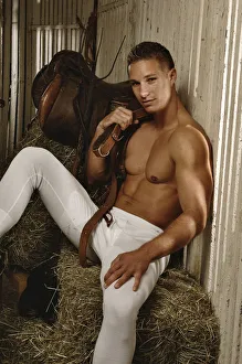 Man with a naked torso wearing long underwear in a horse barn sitting on bales of hay Man with a naked torso wearing long underwear in a horse barn sitting on bales of hay