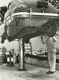 Man repairing uplifted car, (B&W), low section Man repairing uplifted car, (B&W), low section
