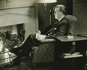 Man sitting on armchair in front of fireplace, (B&W) Man sitting on armchair in front of fireplace, (B&W)