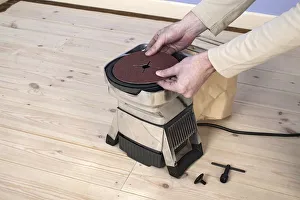 Man using hands to position circle of sand paper on edging sander Man using hands to position circle of sand paper on edging sander
