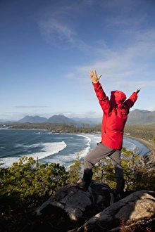 A Man Wearing A Red Jacket Looks Out At The View Of Cox Bay Near Tofino With Arms Raised A Man Wearing A Red Jacket Looks Out At The View Of Cox Bay Near Tofino With Arms Raised