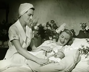 Mother lying in bed smiling to baby-child (0-6 months), nurse standing beside, (B&W) Mother lying in bed smiling to baby-child (0-6 months), nurse standing beside, (B&W)