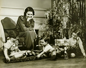 Mother watching three children playing by Christmas tree, (B&W) Mother watching three children playing by Christmas tree, (B&W)