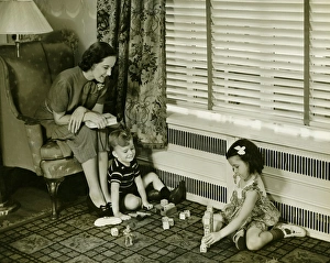 Mother watching over son and daughter (4-5) playing in living room, (B&W) Mother watching over son and daughter (4-5) playing in living room, (B&W)