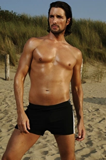 Muscular man wearing swimming trunks posing on beach Muscular man wearing swimming trunks posing on beach