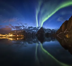 Northern lights over fishing village with mountain range on coastline at Hamnoy Northern lights over fishing village with mountain range on coastline at Hamnoy