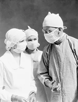 Two nurses and one doctor wearing surgical masks and gowns, looking at one another Two nurses and one doctor wearing surgical masks and gowns, looking at one another