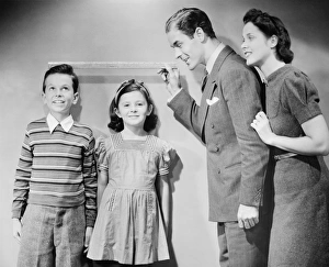 Parents measuring children standing against wall, boy (8-9) girl (6-7), (B&W) Parents measuring children standing against wall, boy (8-9) girl (6-7), (B&W)