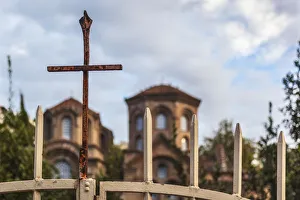 A rusty cross on a gate in front of a church A rusty cross on a gate in front of a church