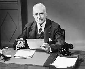 Senior businessman posing at desk in office (B&W), portrait Senior businessman posing at desk in office (B&W), portrait