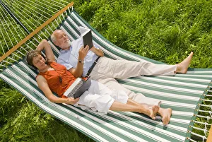 Senior citizen couple lying in a hammock, woman wearing a headset looking at a netbook or Senior citizen couple lying in a hammock, woman wearing a headset looking at a netbook or