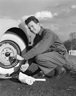 Images Dated 10th February 2006: Smiling man in coveralls using tire iron to change tire on sedan