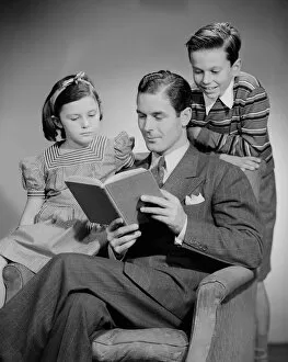 Legs Crossed At Knee Gallery: Studio shot of father with two children (10-11) reading book