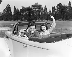Images Dated 10th February 2006: Teenage couple in convertible car smile and wave to viewer