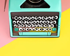 <b class=qtipBold><figcaption>Typewriter with googly eyes for keys</figcaption></b><br>Top down view of a turquoise colored vintage typewriter with googly eyes for keys on a pink and yellow color blocked background.<br><em>© JUJ WINN 2018</em> Typewriter with googly eyes for keys