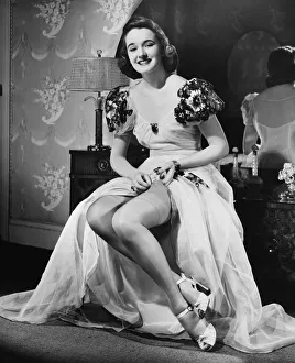 Woman in evening gown putting on stockings at vanity table (B&W), portrait Woman in evening gown putting on stockings at vanity table (B&W), portrait
