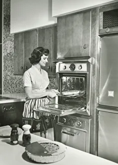 Woman putting meal into oven in kitchen, (B&W) Woman putting meal into oven in kitchen, (B&W)