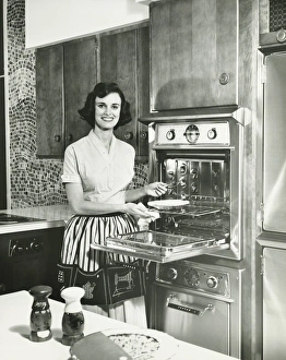 Woman putting pie into oven in kitchen, (B&W), portrait Woman putting pie into oven in kitchen, (B&W), portrait