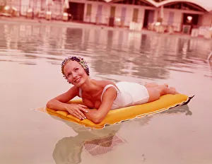 Sports Venue Gallery: Woman in swimming pool reclining on inflatable raft, wearing bathing cap, smiling