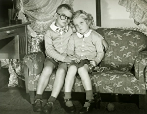 Young boy and girl dressed as adults sitting on sofa, portrait Young boy and girl dressed as adults sitting on sofa, portrait