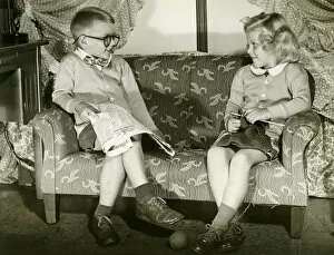 Legs Crossed At Knee Gallery: Young boy and girl sitting on sofa, imitating married couple