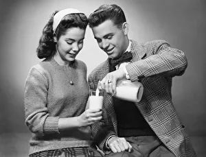 Young couple pouring milk from bottle to glass in studio, (B&W) Young couple pouring milk from bottle to glass in studio, (B&W)