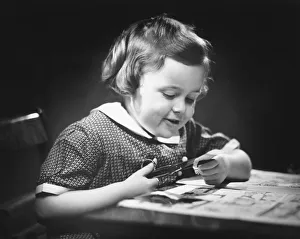 Young girl (4-5) at table cutting paper with scissors, (B&W), close-up Young girl (4-5) at table cutting paper with scissors, (B&W), close-up