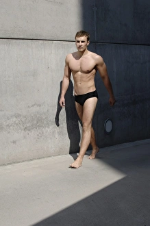 Young man wearing bathing trunks, walking in front of a concrete wall Young man wearing bathing trunks, walking in front of a concrete wall