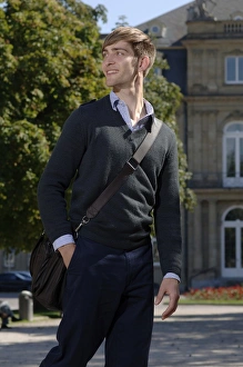 Young man wearing elegant clothing with a bag over his shoulder in front of the New Young man wearing elegant clothing with a bag over his shoulder in front of the New