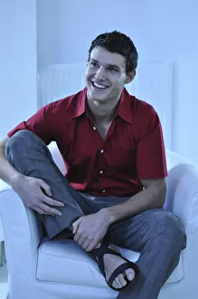 Young man wearing a red shirt sitting in an armchair, smiling Young man wearing a red shirt sitting in an armchair, smiling