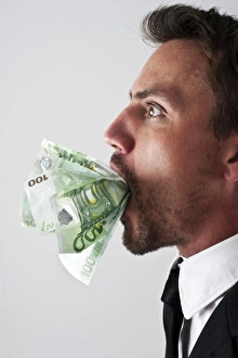 Young man wearing a suit with 100-euro notes stuffed into his mouth Young man wearing a suit with 100-euro notes stuffed into his mouth