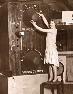 Images Dated 30th August 2005: Young woman, standing on chair, adjusting giant radio tuner (B&W)