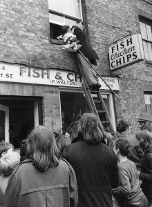The bridegroom climbs a ladder to kiss his bride at the window above a fish and chip shop The bridegroom climbs a ladder to kiss his bride at the window above a fish and chip shop