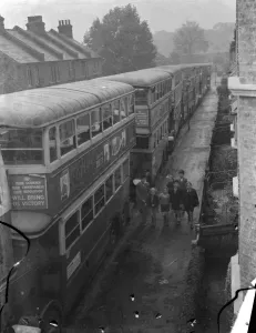 A group of children walking past a seriers of London Transport buses which are parked A group of children walking past a seriers of London Transport buses which are parked