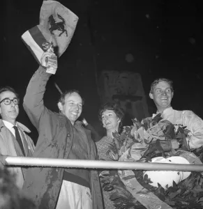 John Surtees smiles as he waves his trophy from the Victory Rostrum after he had John Surtees smiles as he waves his trophy from the Victory Rostrum after he had