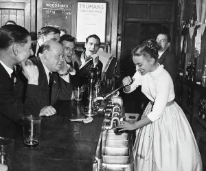 A woman barmaid pulls a pint of beer for male customers in a London pub , England. 1950s A woman barmaid pulls a pint of beer for male customers in a London pub , England. 1950s