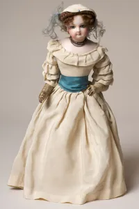 Bisque fashion doll with swivel head, wearing a long cream dress and hat Bisque fashion doll with swivel head, wearing a long cream dress and hat