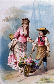 Little gardener: a young boy with a wheelbarrow full of flowers talks with a young woman