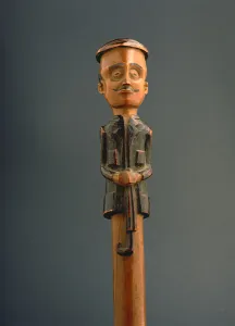Stick with a figure of a European man wearing a cap and holding an umbrella, Ovimbundu Stick with a figure of a European man wearing a cap and holding an umbrella, Ovimbundu