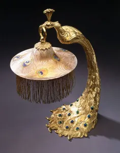 A table lamp with the base cast as a peacock holding the glass shade from its mouth, c A table lamp with the base cast as a peacock holding the glass shade from its mouth, c