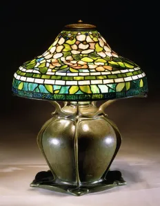 A table lamp with a waisted conical shade, with pink blossoms amongst green leaves A table lamp with a waisted conical shade, with pink blossoms amongst green leaves