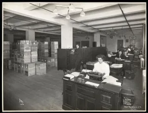 View of men and women at desks in what appears to be a shipping room at Parke, Davis & Co View of men and women at desks in what appears to be a shipping room at Parke, Davis & Co