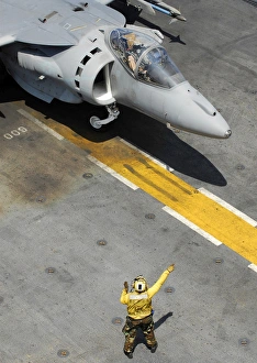 An Airman uses hand signals to direct an AV-8B Harrier during flight operations aboard An Airman uses hand signals to direct an AV-8B Harrier during flight operations aboard