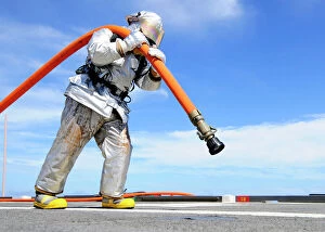 Firefighter carries a charged hose across the flight deck of USS Denver