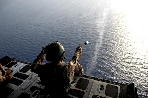A loadmaster throws a smoke grenade out of an HC-130 aircraft A loadmaster throws a smoke grenade out of an HC-130 aircraft