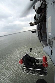 Naval Air Crewman hoists a rescue basket into an MH-60S Sea Hawk helicopter Naval Air Crewman hoists a rescue basket into an MH-60S Sea Hawk helicopter