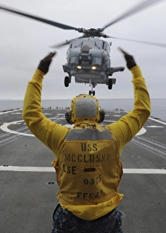 Petty Officer guides an SH-60R Sea Hawk helicopter onto the flight deck of USS McClusky Petty Officer guides an SH-60R Sea Hawk helicopter onto the flight deck of USS McClusky