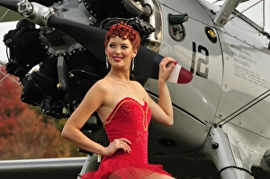 Redhead pin-up girl in 1940s style dancer attire holding on to a vintage aircraft Redhead pin-up girl in 1940s style dancer attire holding on to a vintage aircraft